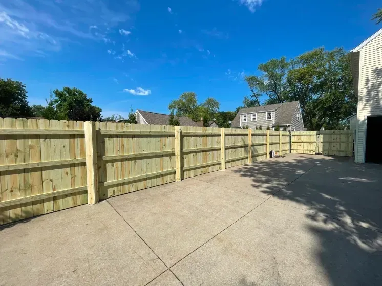 Empty paved area beside a wooden fence under a bright blue sky