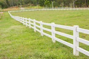 White fence curving through a grassy field under a cloudy sky