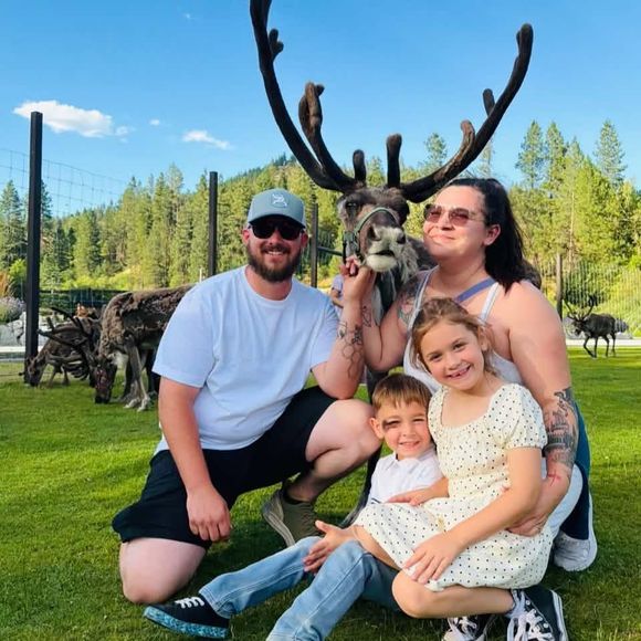 Family posing with a reindeer outdoors on a sunny grassy field.