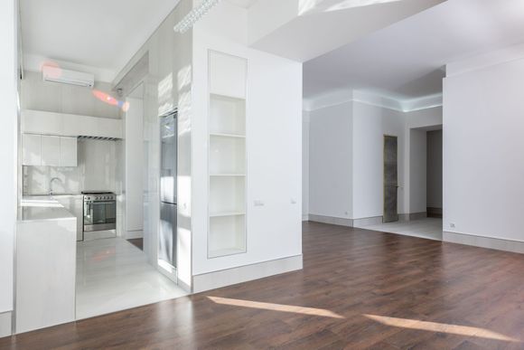 Bright empty modern apartment with white kitchen, wood floors, and large open living area
