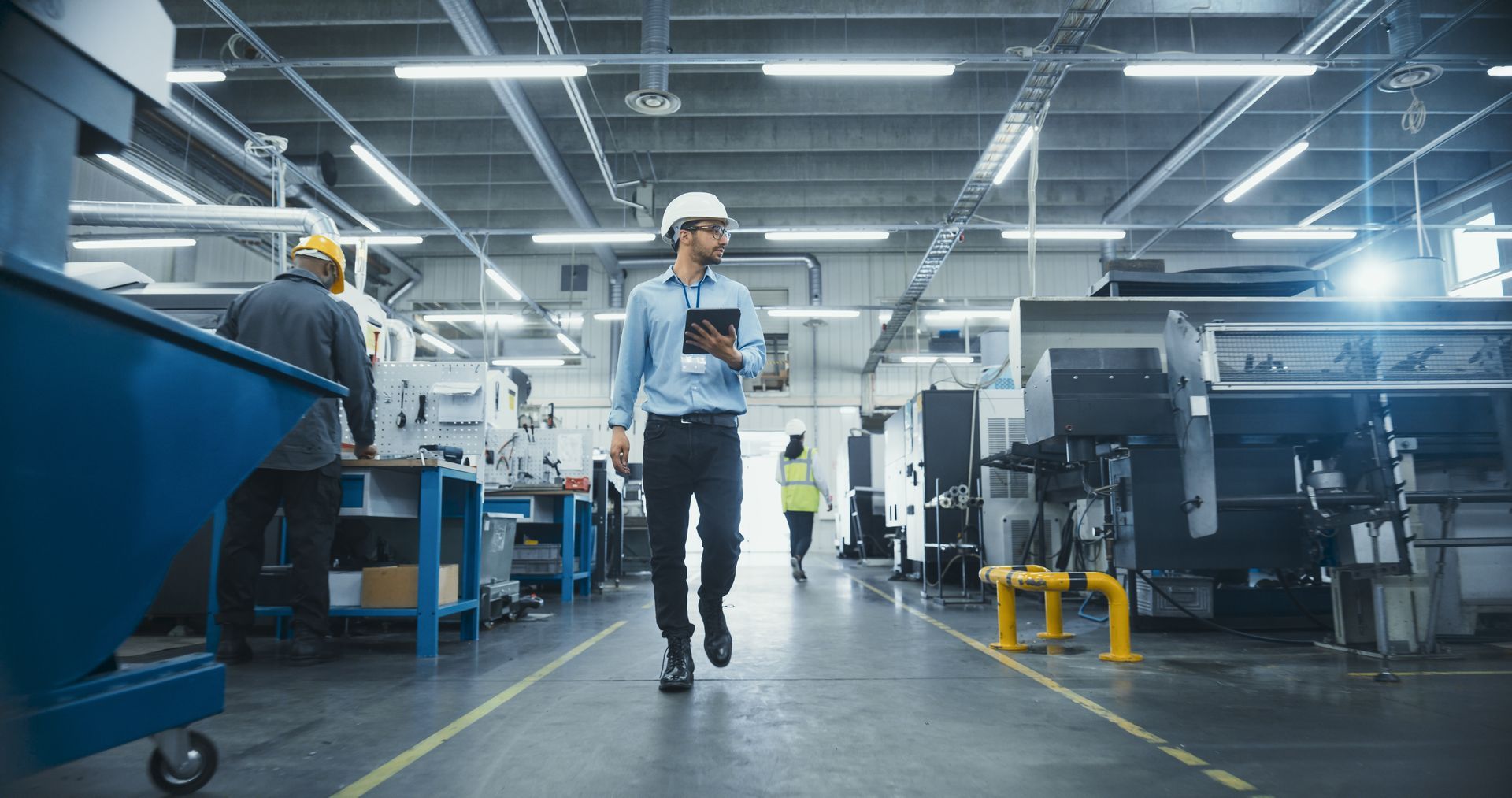 Worker in hard hat walking through a factory aisle between large industrial machines.