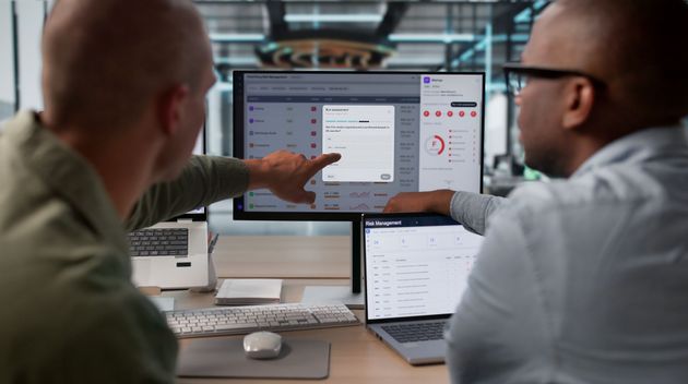 Two coworkers review analytics on a desktop monitor in a modern office. Two coworkers review analytics on a desktop monitor in a modern office.
