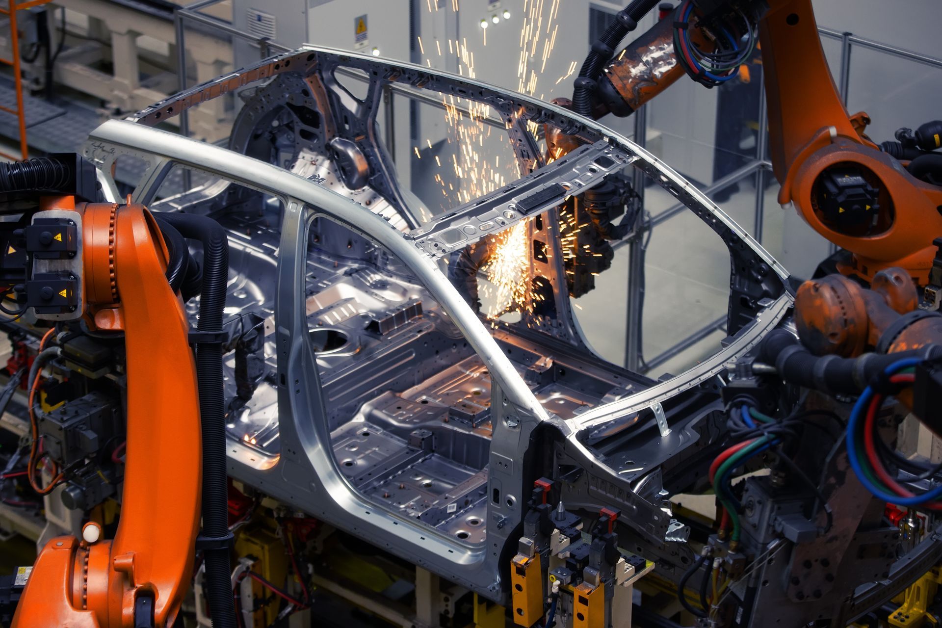 Robotic arms welding a silver car body on an assembly line, sparks flying in an ավտomated factory