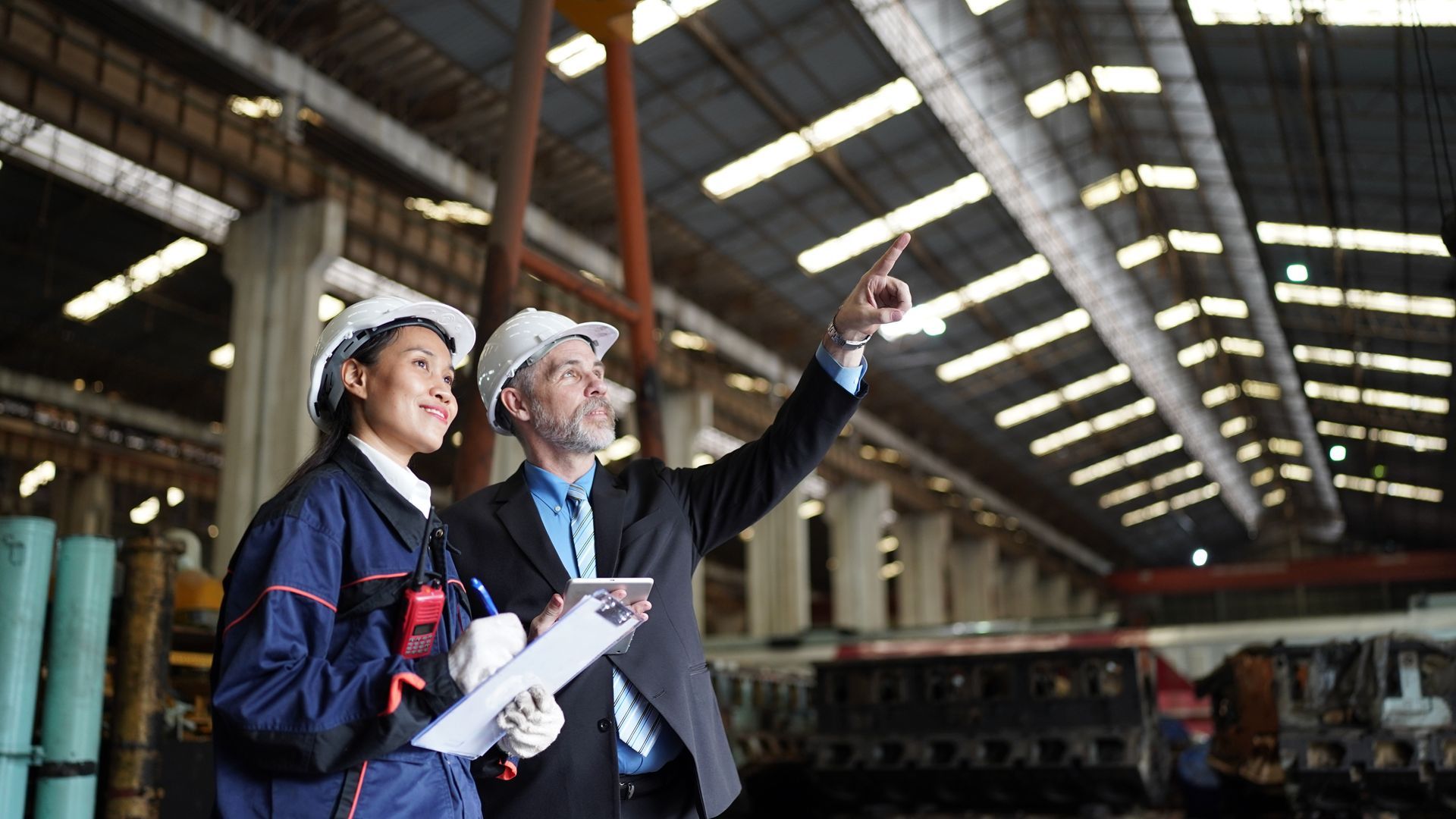Two workers in hard hats inspect machinery inside a large industrial warehouse