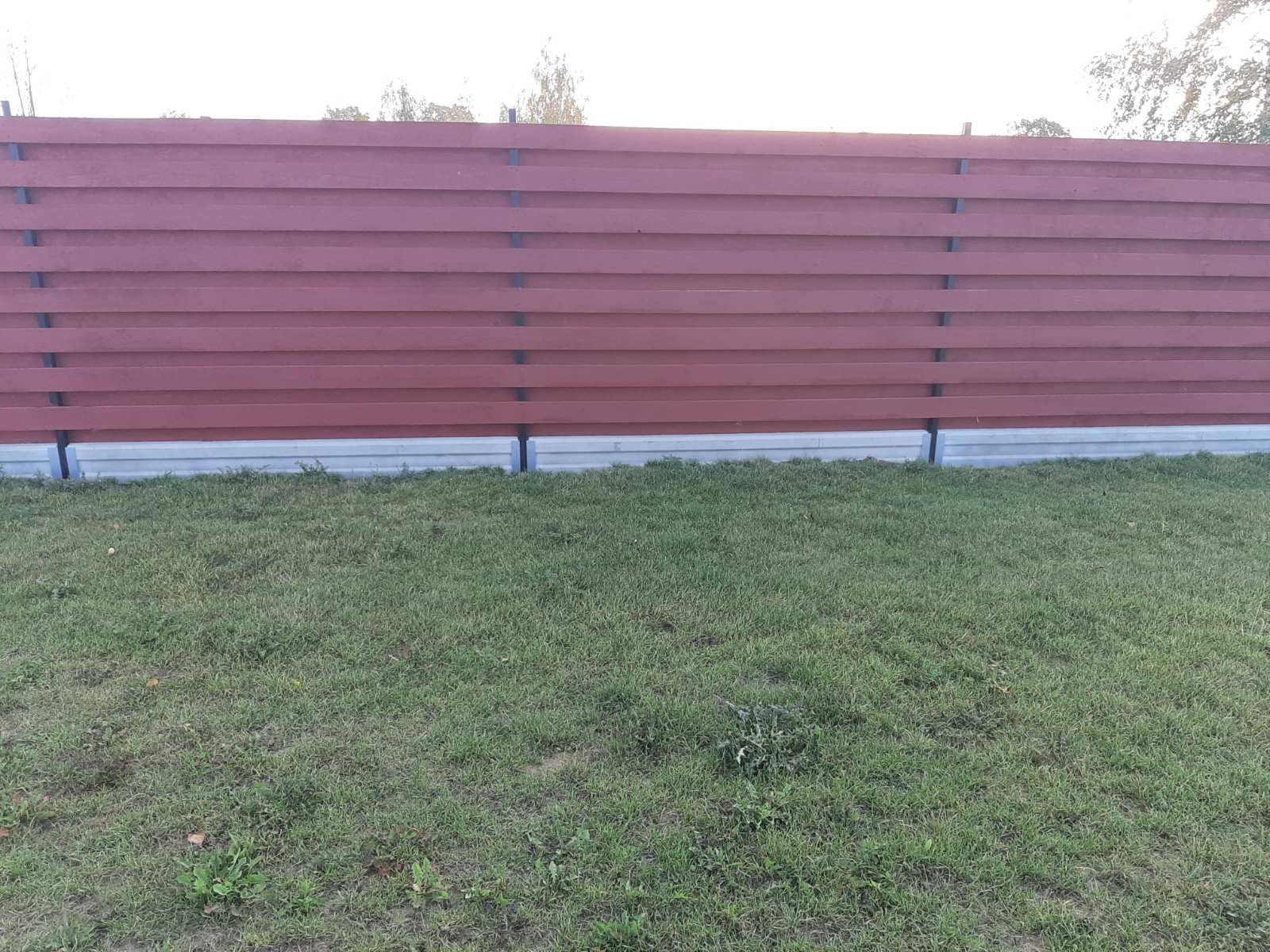 Žalio lauko viduryje stovi raudona medinė tvora.