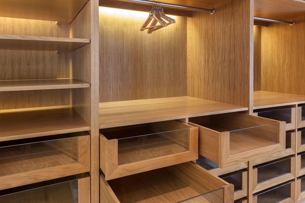 Cabina armadio vuota in legno, con ripiani, aste appendiabiti e cassetti, illuminata da una luce calda