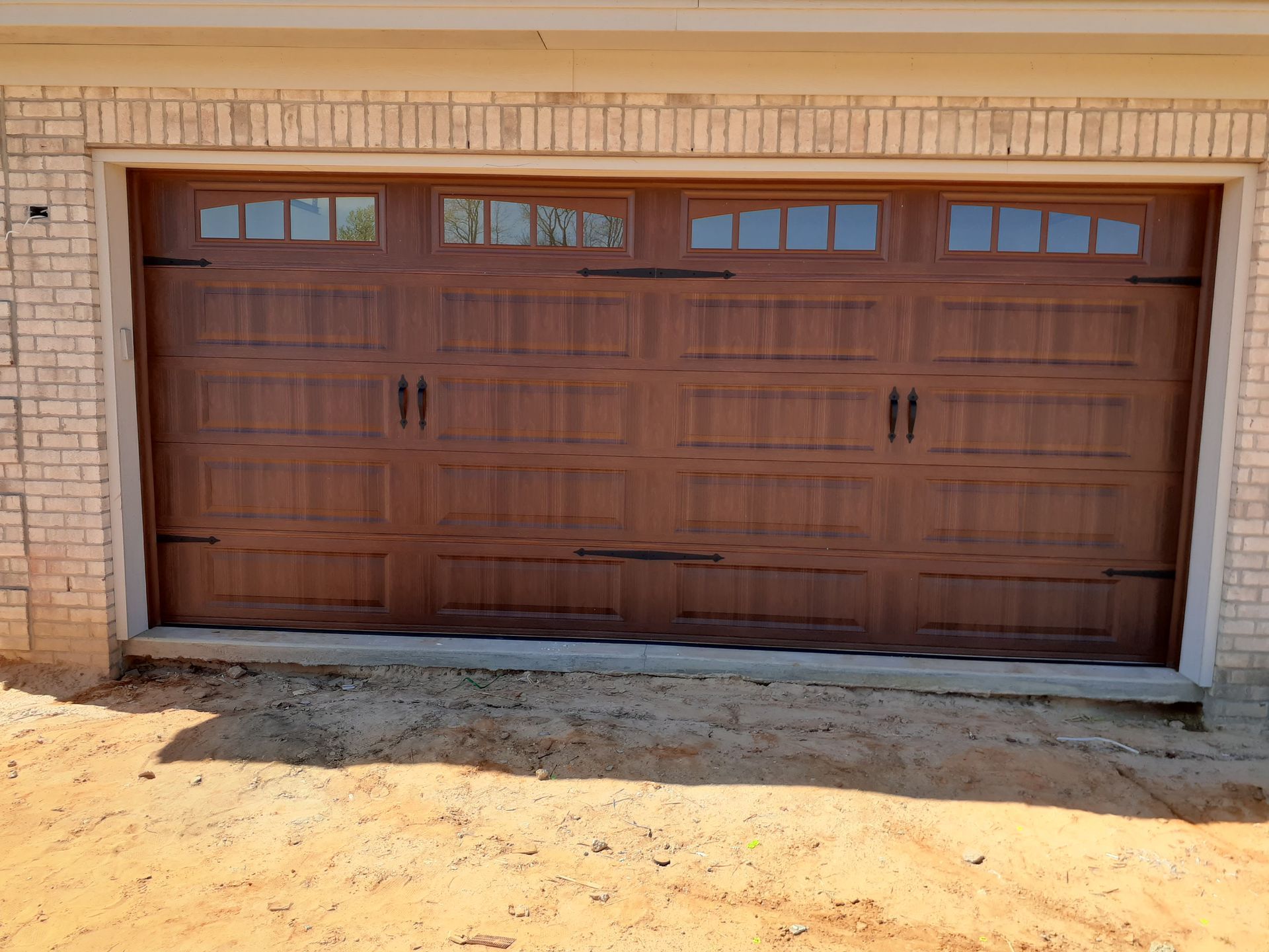 Brown garage door with windows, handles, and hinges. Brick exterior with sandy ground in Lumberton, NC.