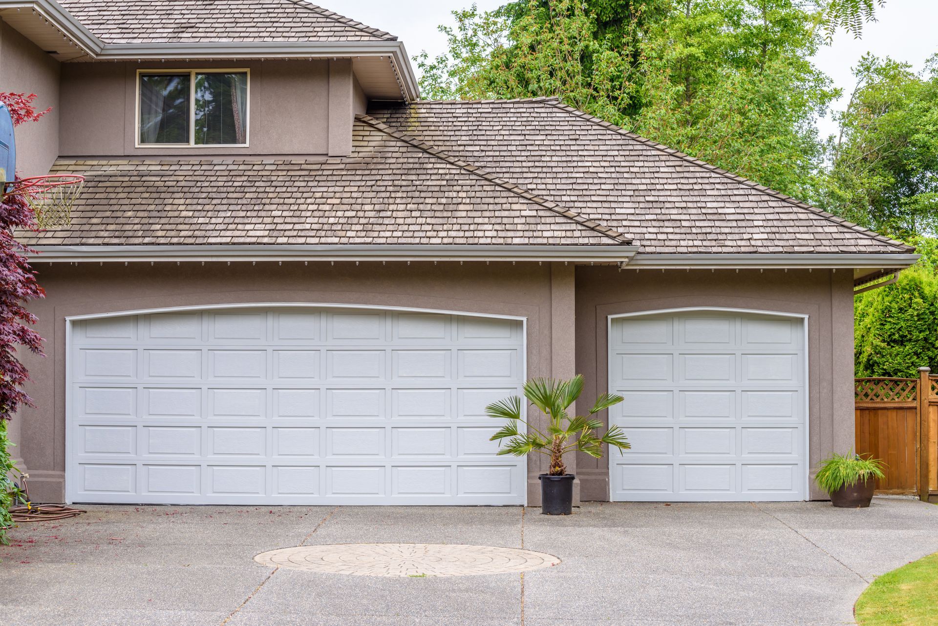 a large house with two white garage doors and a wooden fence .