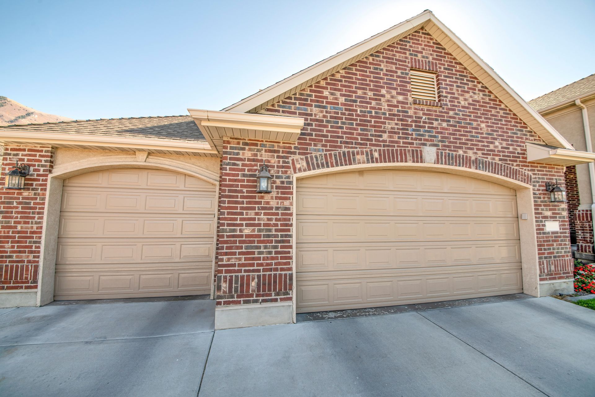 a brick house with two tan garage doors and a concrete driveway .