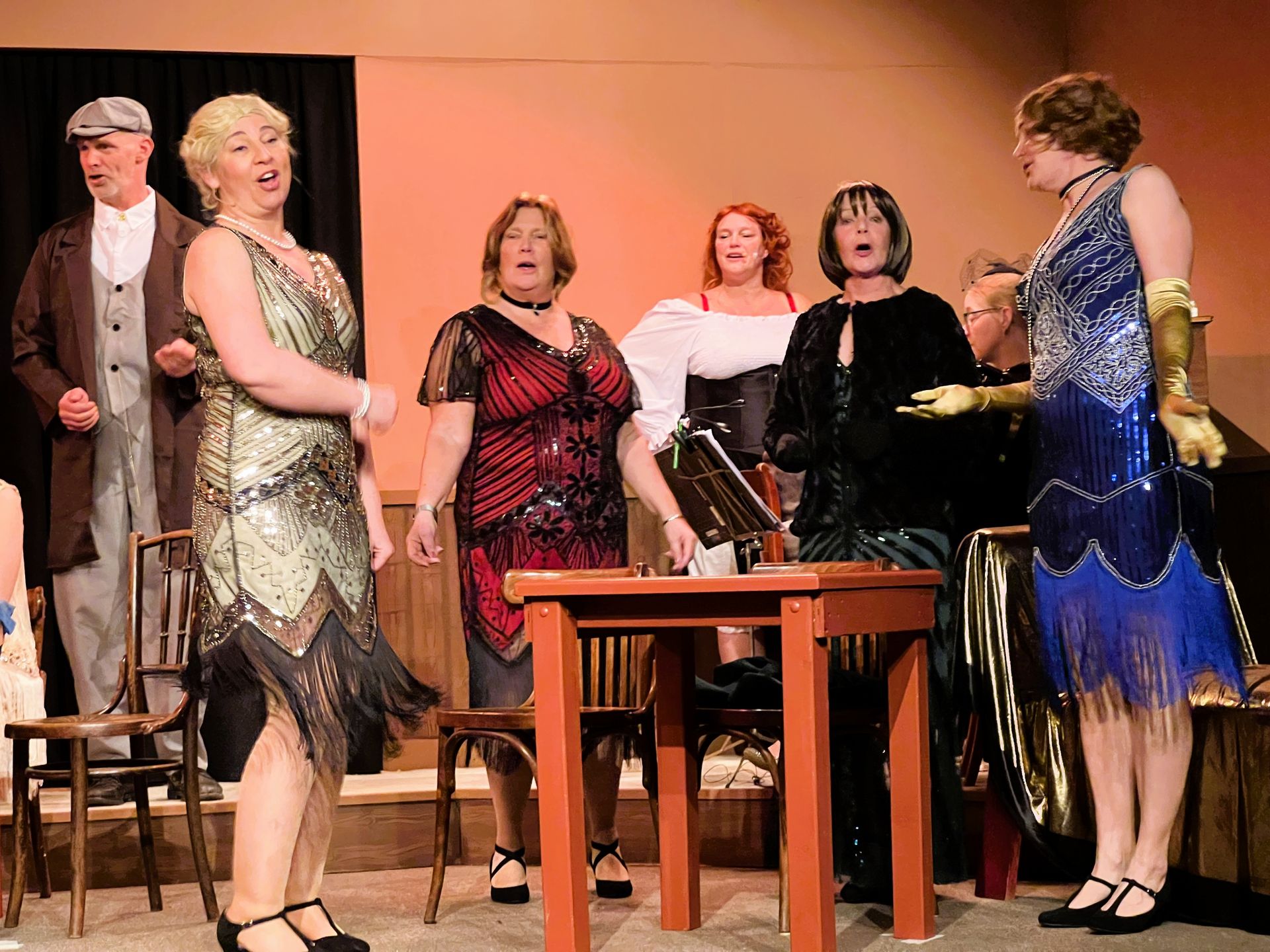 Rooie Sien. Een theatervoorstelling met acteurs in kostuums, sommigen zingen, op een podium met een tafel.