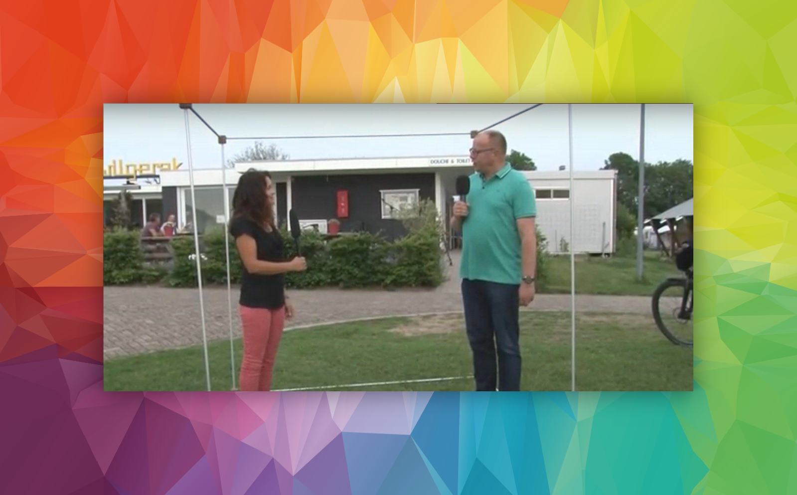 Twee personen bevinden zich in een open constructie van een kubus, waarvan ƩƩn een microfoon vasthoudt.