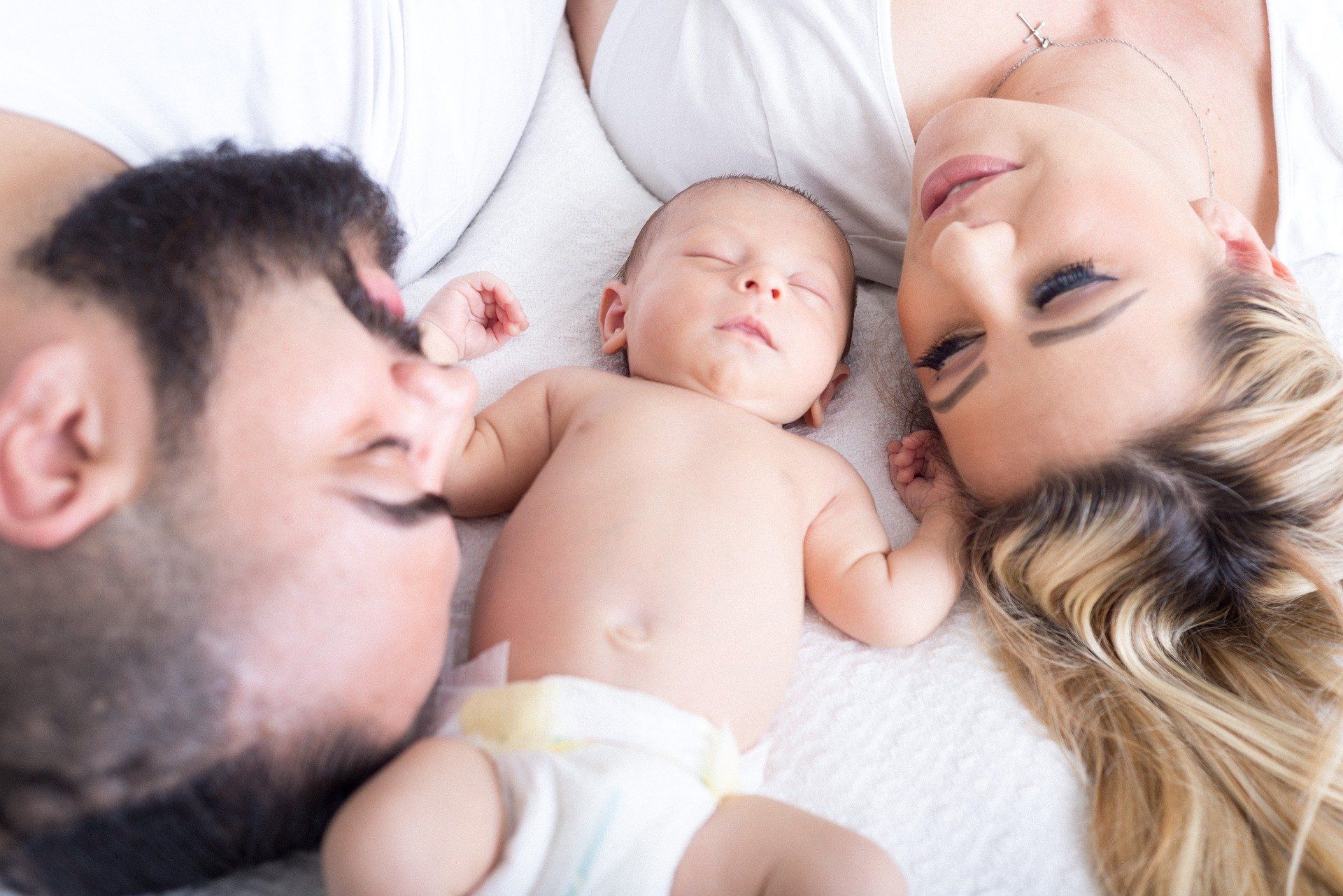 Ouders liggen aan weerszijden van een pasgeboren baby, allen slapend op een witte ondergrond.