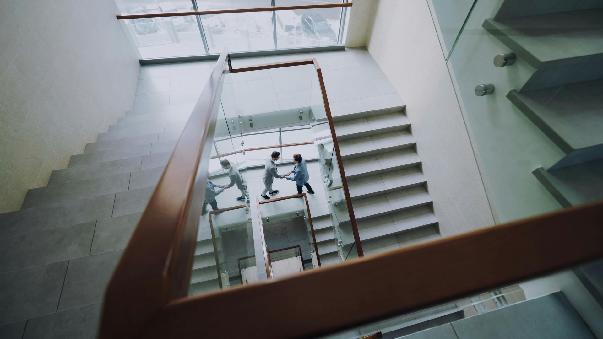 High-angle view of two people shaking hands on a modern, brightly lit interior staircase.