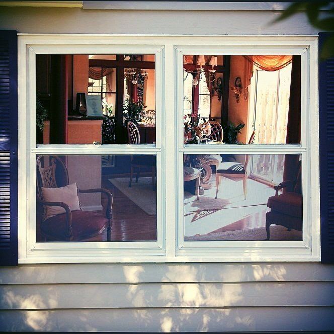 A living room is reflected in a window with blue shutters