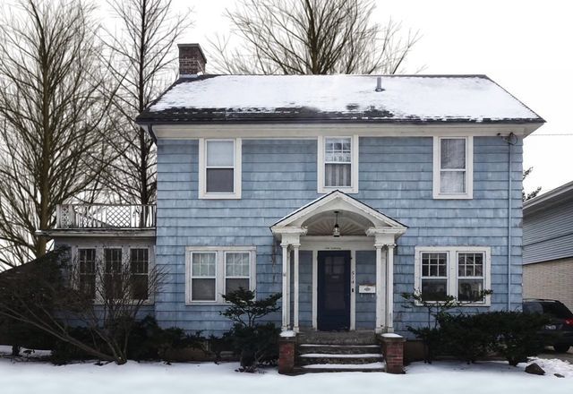 A blue house with snow on the roof and trees in the background