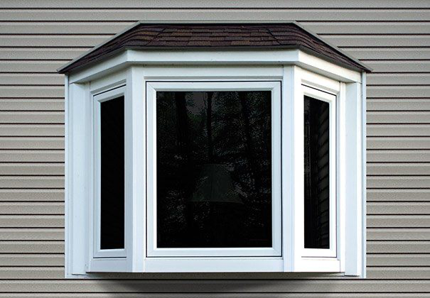A white bay window with a brown roof is on the side of a house.