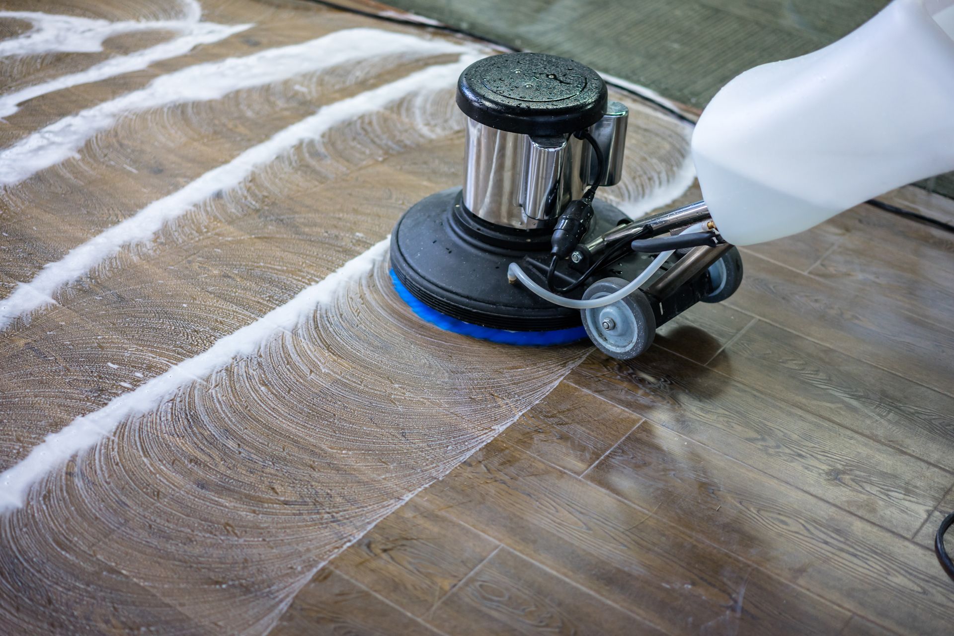 Floor-cleaning machine scrubbing a wooden surface with white foam lines