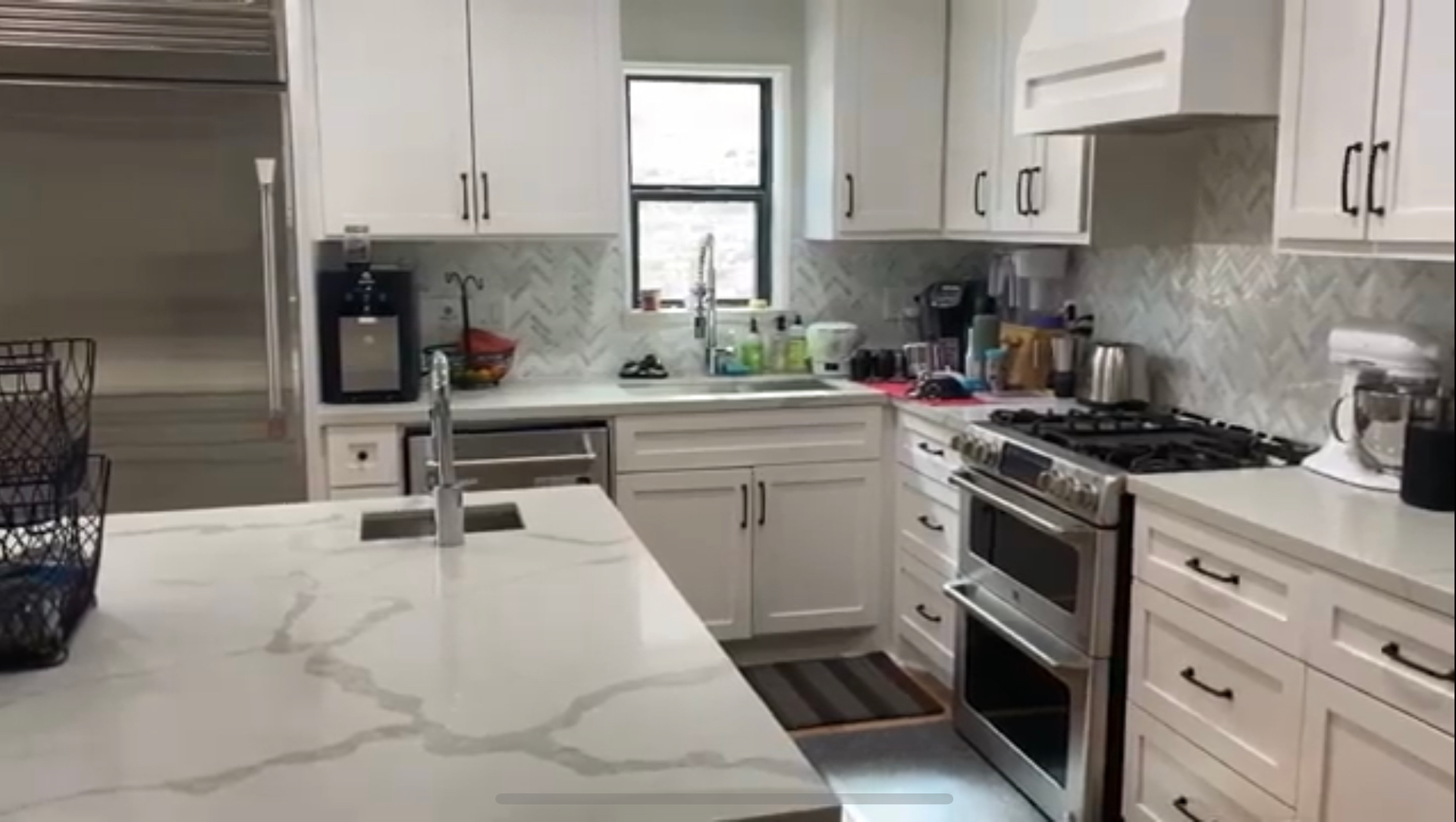 A bright, modern kitchen featuring white cabinets, a marble-topped island, 