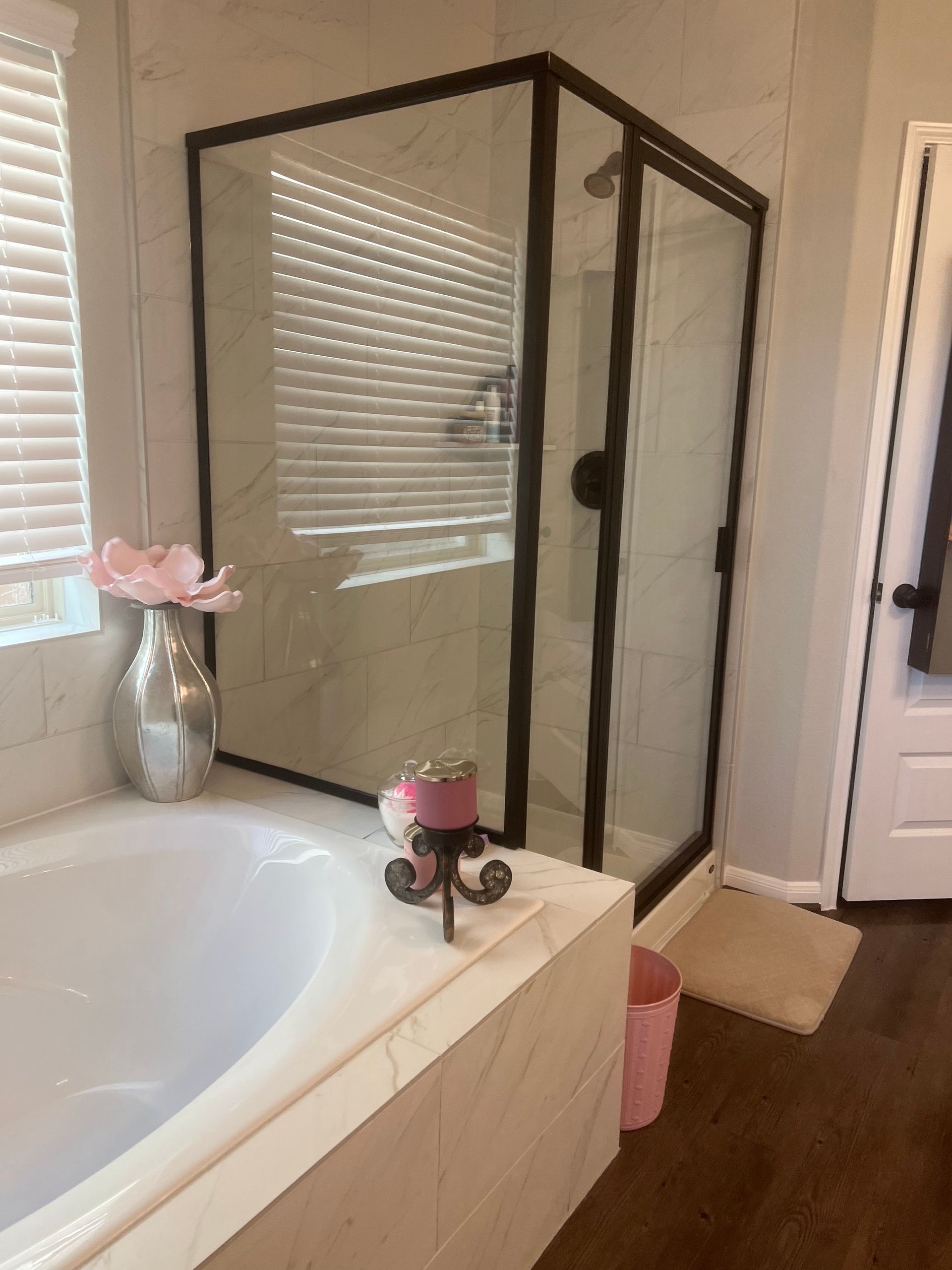 A modern bathroom featuring a white soaking tub, a corner glass shower with black framing, and neutral tile flooring.