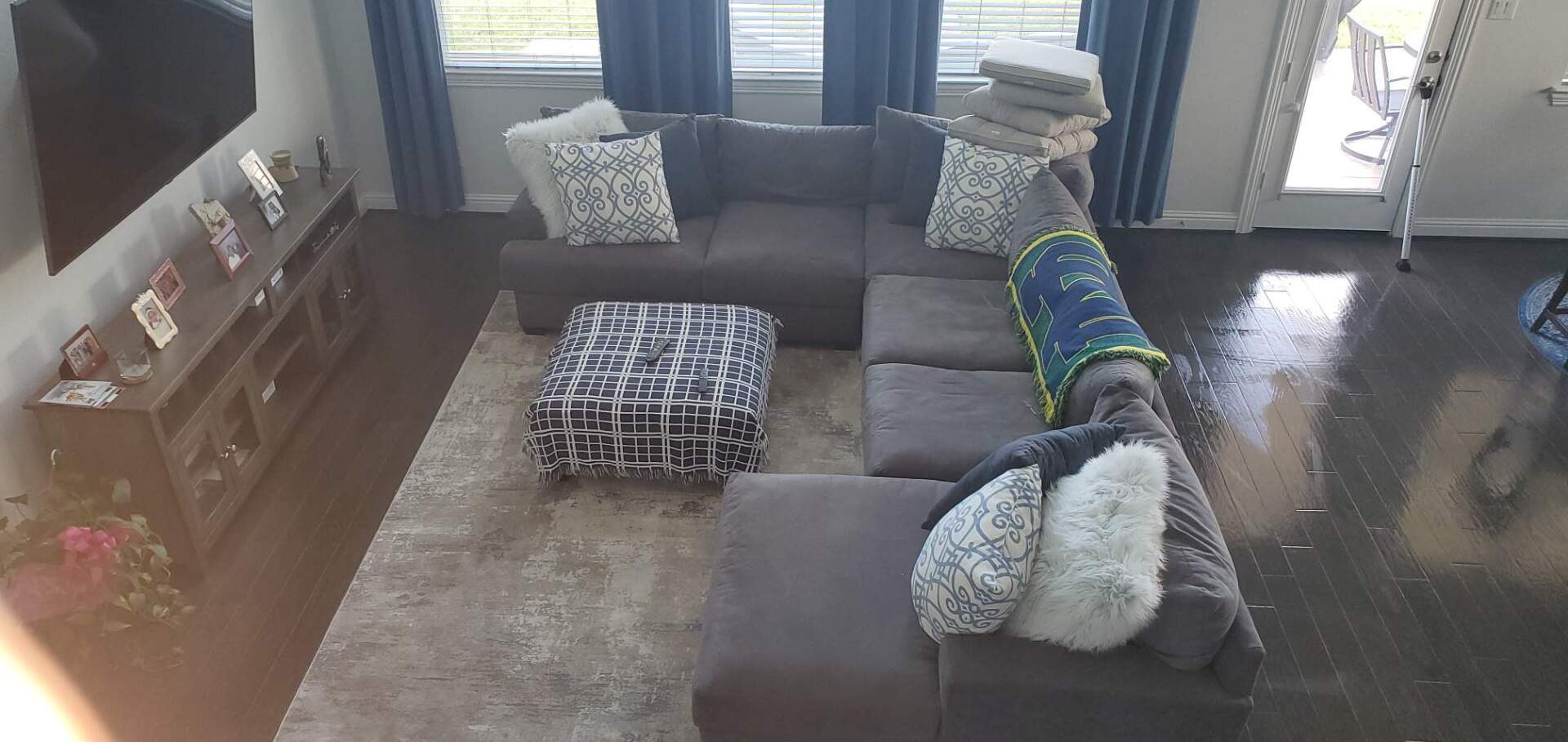 An overhead view of a living room featuring a grey sectional sofa, patterned ottoman, area rug, and wood media console.