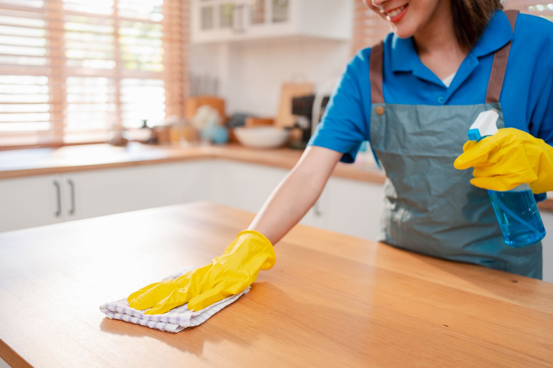A female worker is cleaning a kitchen counter with cloth and spray bottle A female worker is cleaning a kitchen counter with cloth and spray bottle