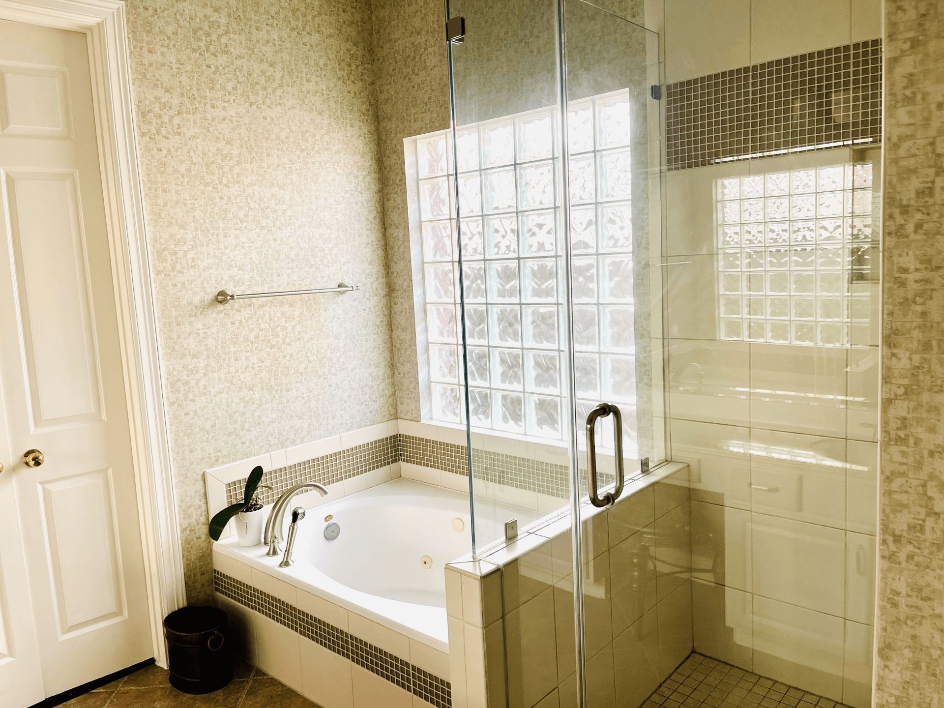 Bathroom featuring a white jetted bathtub, a glass-enclosed shower, and a glass block window with patterned wallpaper.