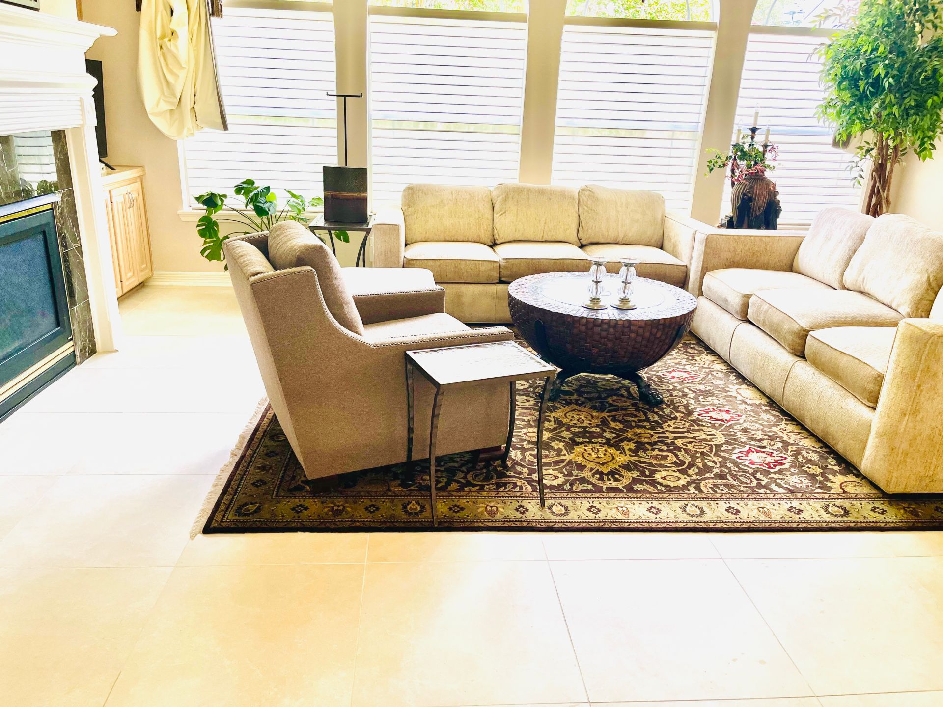 A cozy living room with a beige sofa, matching armchair, circular coffee table, and patterned rug on a tiled floor.