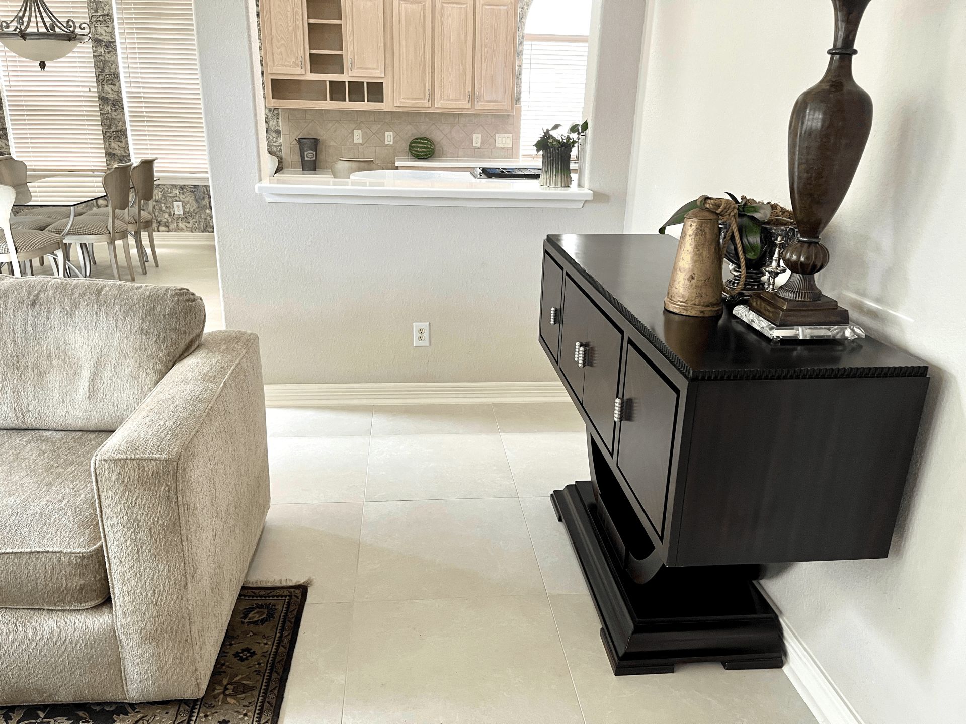 A dark wood console table sits against a white wall next to a light-colored armchair in a living area with a kitchen pass.