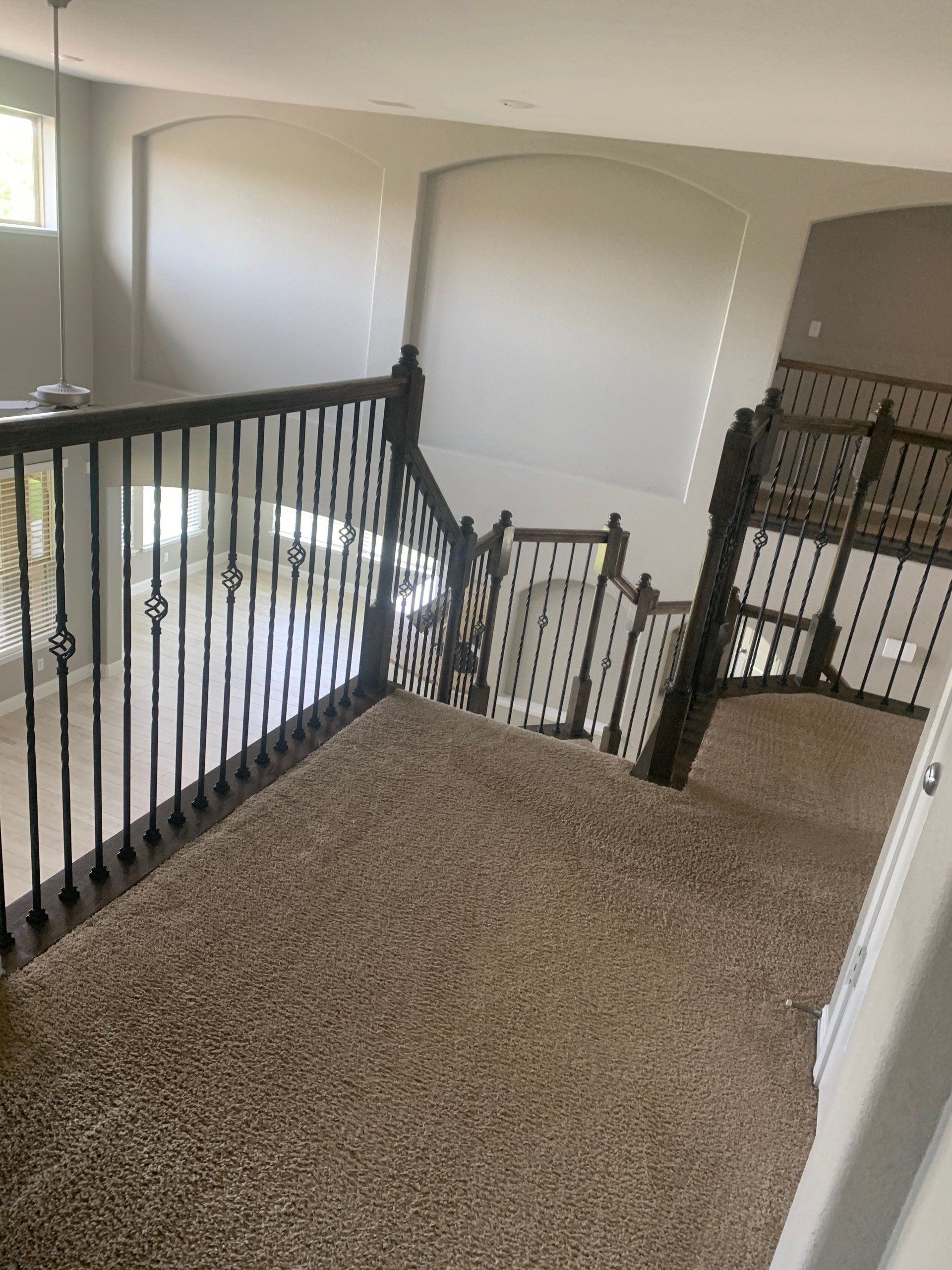Upper-level hallway with carpet, dark wood railings, and views overlooking a lower floor through arched cutouts.