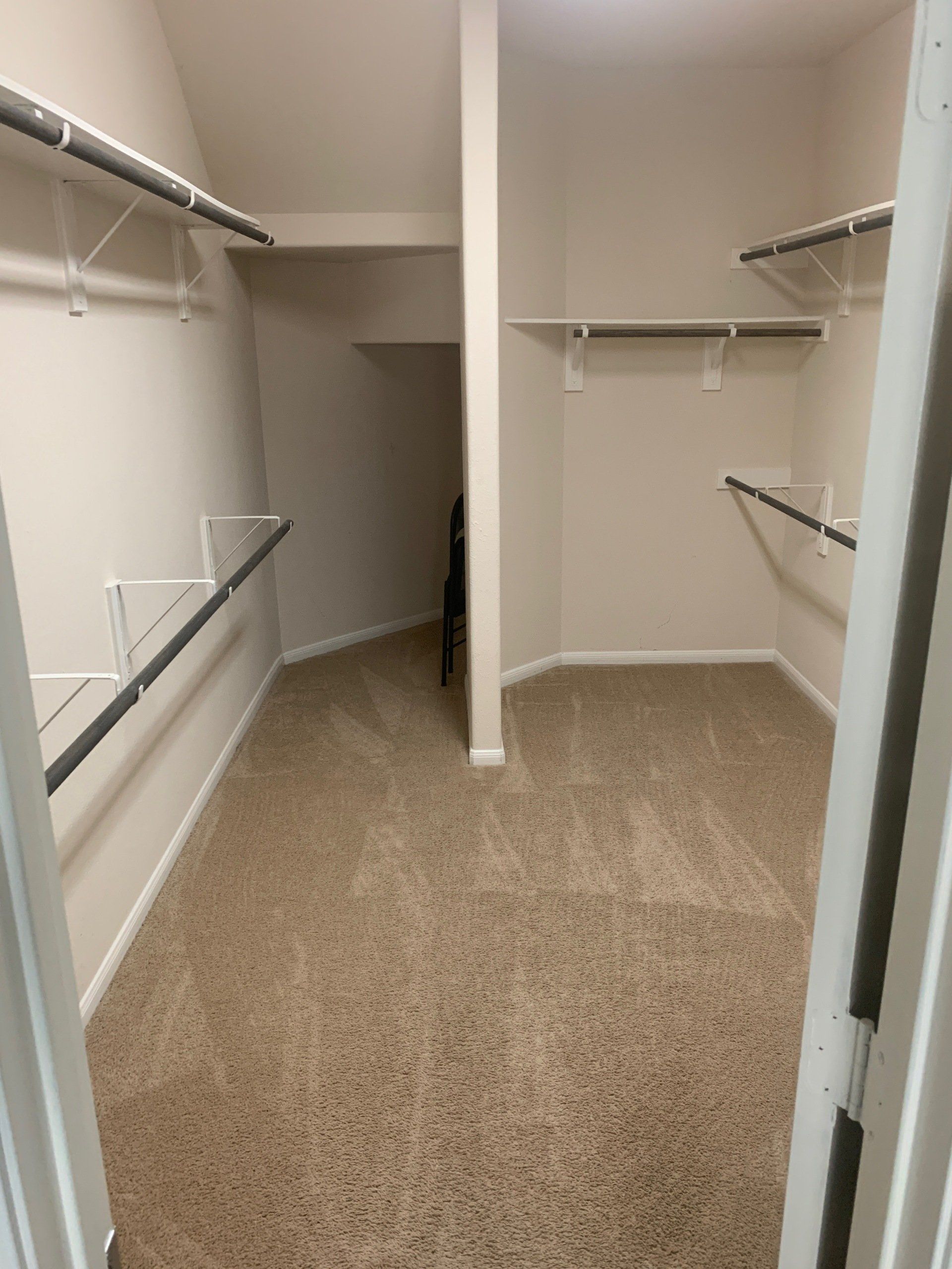An empty walk-in closet with beige carpet, white walls, and multiple tiered wire shelving units for hanging clothes.