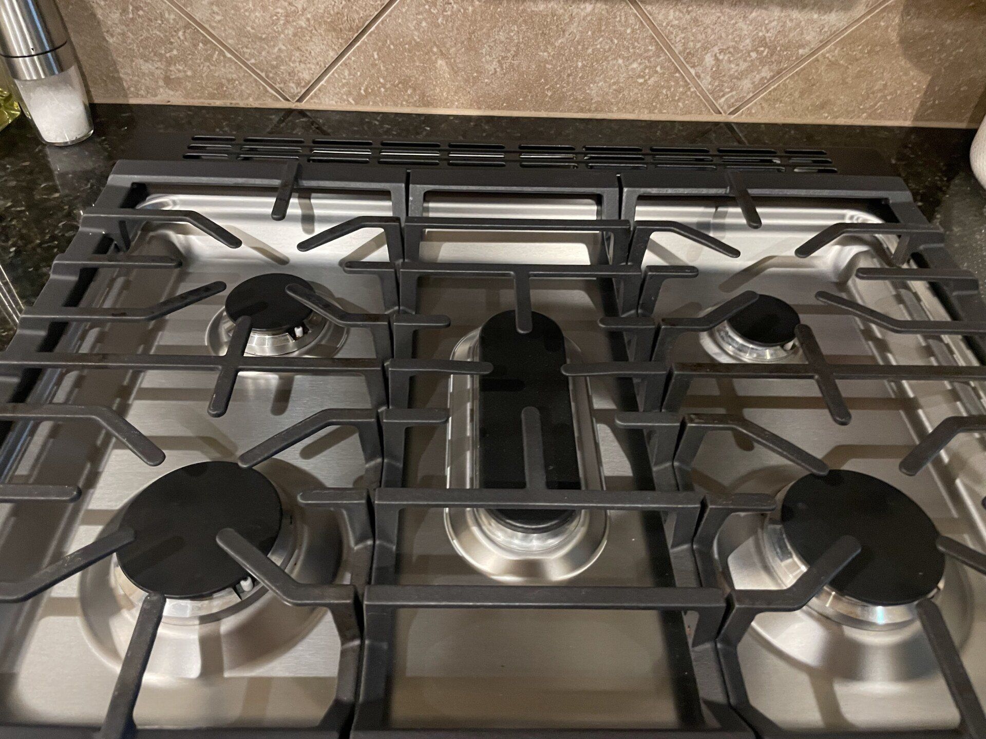 A five-burner stainless steel gas stovetop with heavy cast iron grates on a dark countertop.
