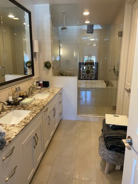 A modern bathroom with a double vanity, marble-style countertops, white cabinetry, and a walk-in glass shower.