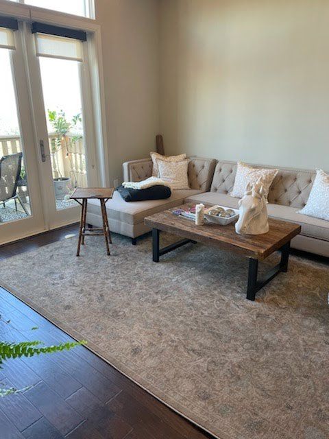 A beige tufted sectional sofa sits on a large, patterned area rug near a glass door in a neutral-toned living room.