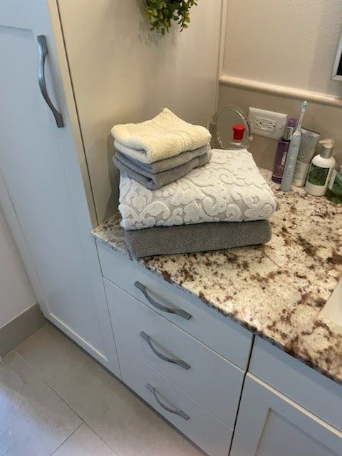 A stack of folded white, grey, and textured towels sitting on a granite bathroom vanity next to toiletries.