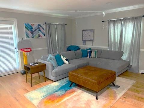 Living room with a gray sectional sofa, leather ottoman, colorful rug, and a yellow basketball hoop stand.