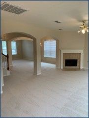A bright, carpeted living room with beige walls, a white fireplace, and arched doorways leading to another room.