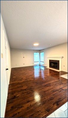Empty living room with dark hardwood floors, white walls, and a fireplace under a vaulted ceiling.