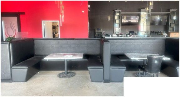 Empty restaurant booths with black leather seating and white tables against a red and dark brown wall.