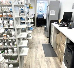 Pharmacy interior with shelving units filled with medication bottles to the left and a computer workstation to the right.