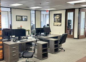 An office workspace featuring two gray desks with computers, black office chairs, and neutral decor.