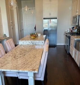 A kitchen with a long granite-topped island and light pink upholstered chairs on a dark wood floor.