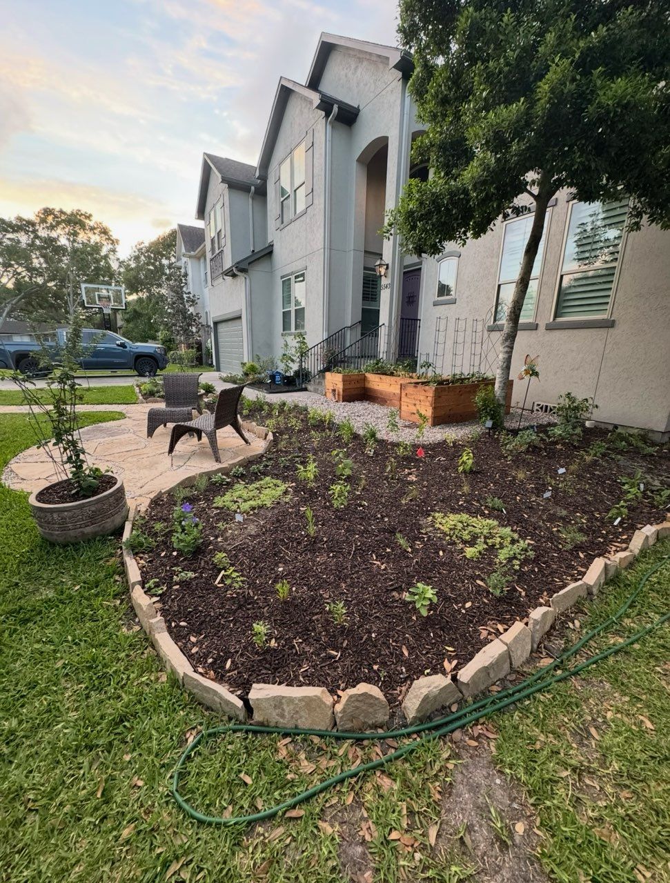 House with landscaped front yard, stone patio with chairs, and raised garden beds.
