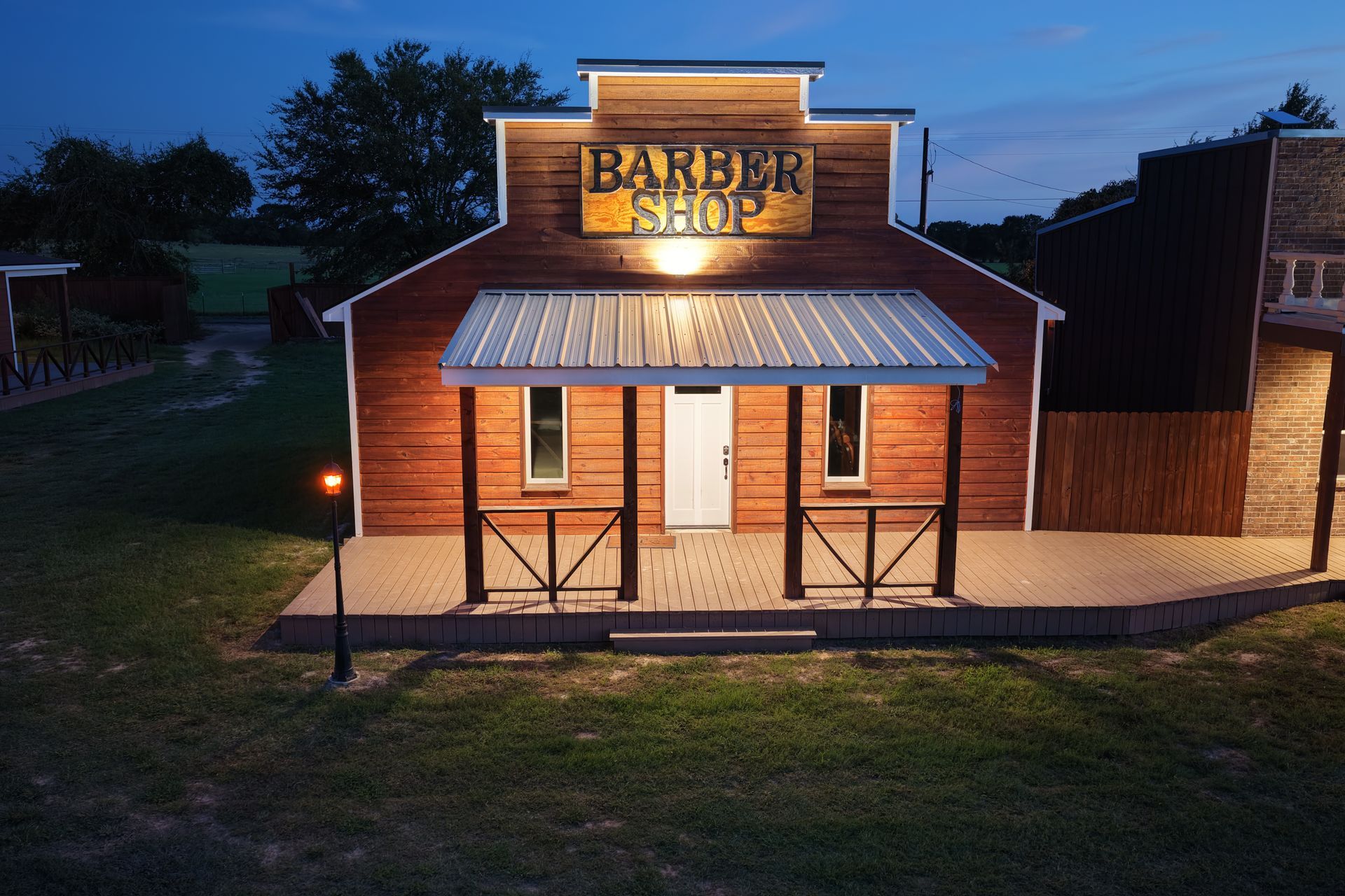 Brick shop building at dusk with a lit porch and sign reading “Barber Shop”