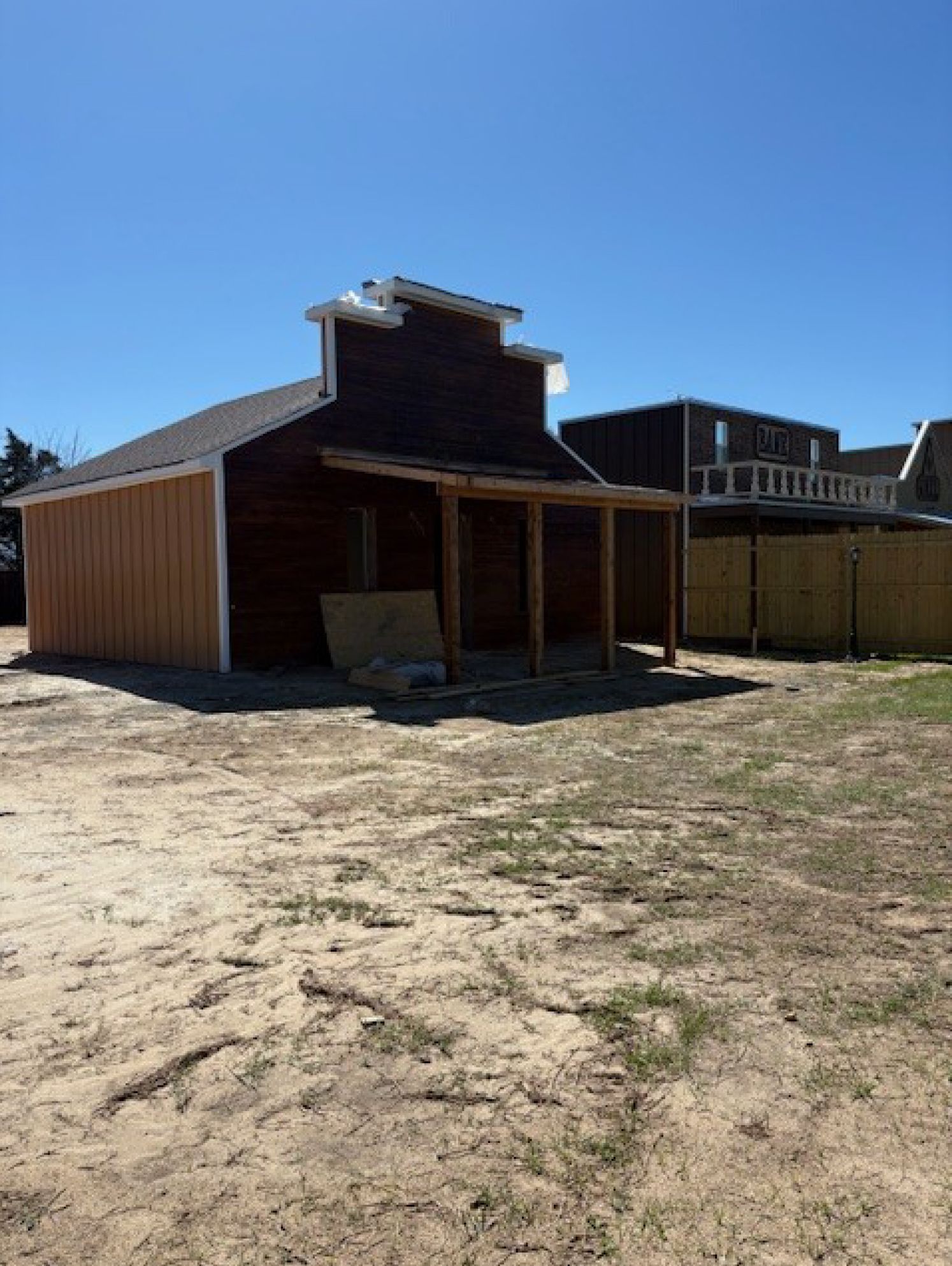 A rustic wooden building under construction with a Western-style false front, standing in a sandy, open lot.