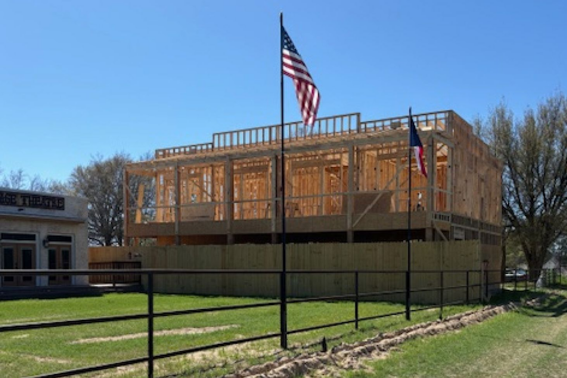 A multi-story wooden building under construction, enclosed by a fence with two American flags flying in front.