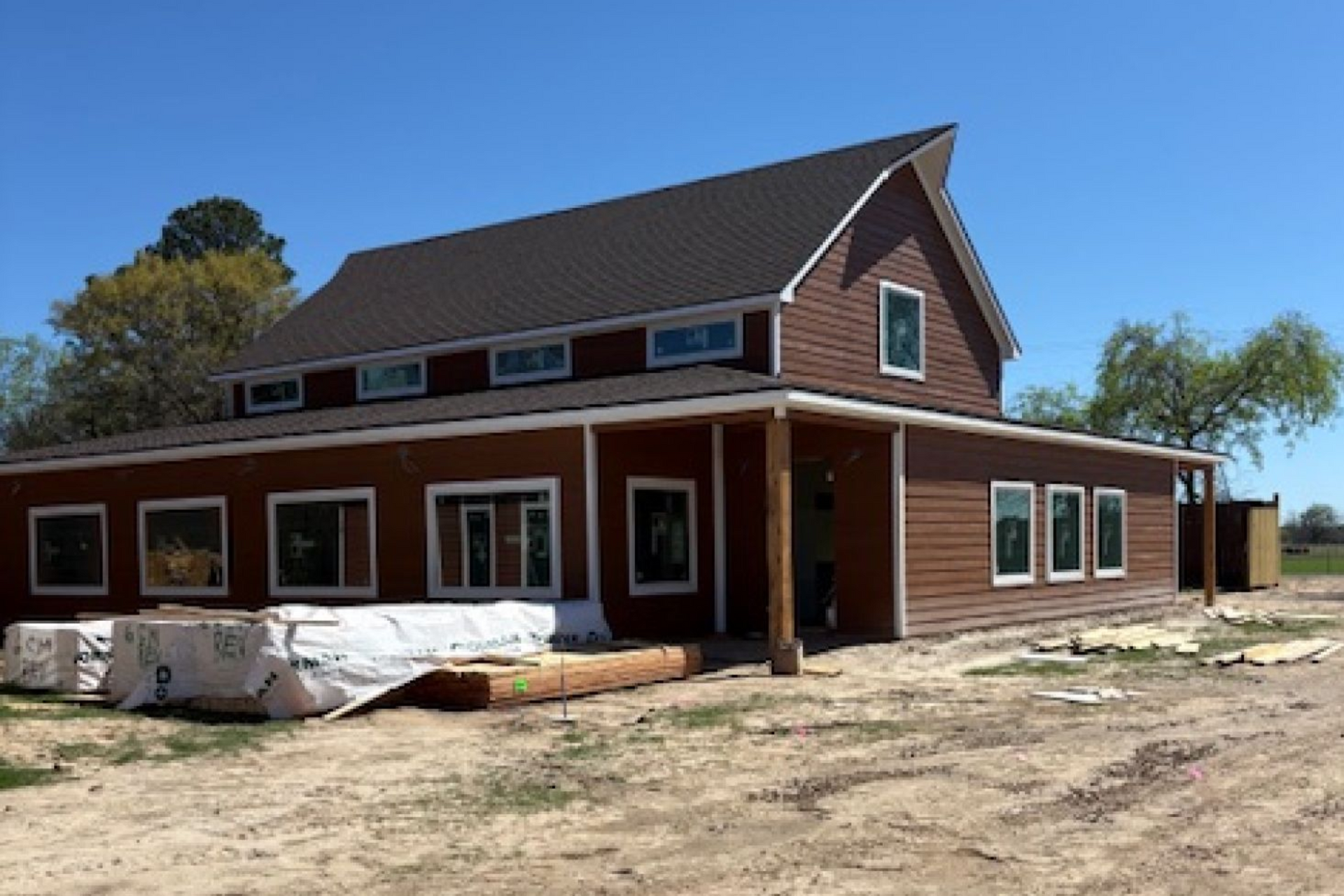 A newly constructed two-story building with dark brown horizontal siding, a dark roof, and a porch under a blue sky.