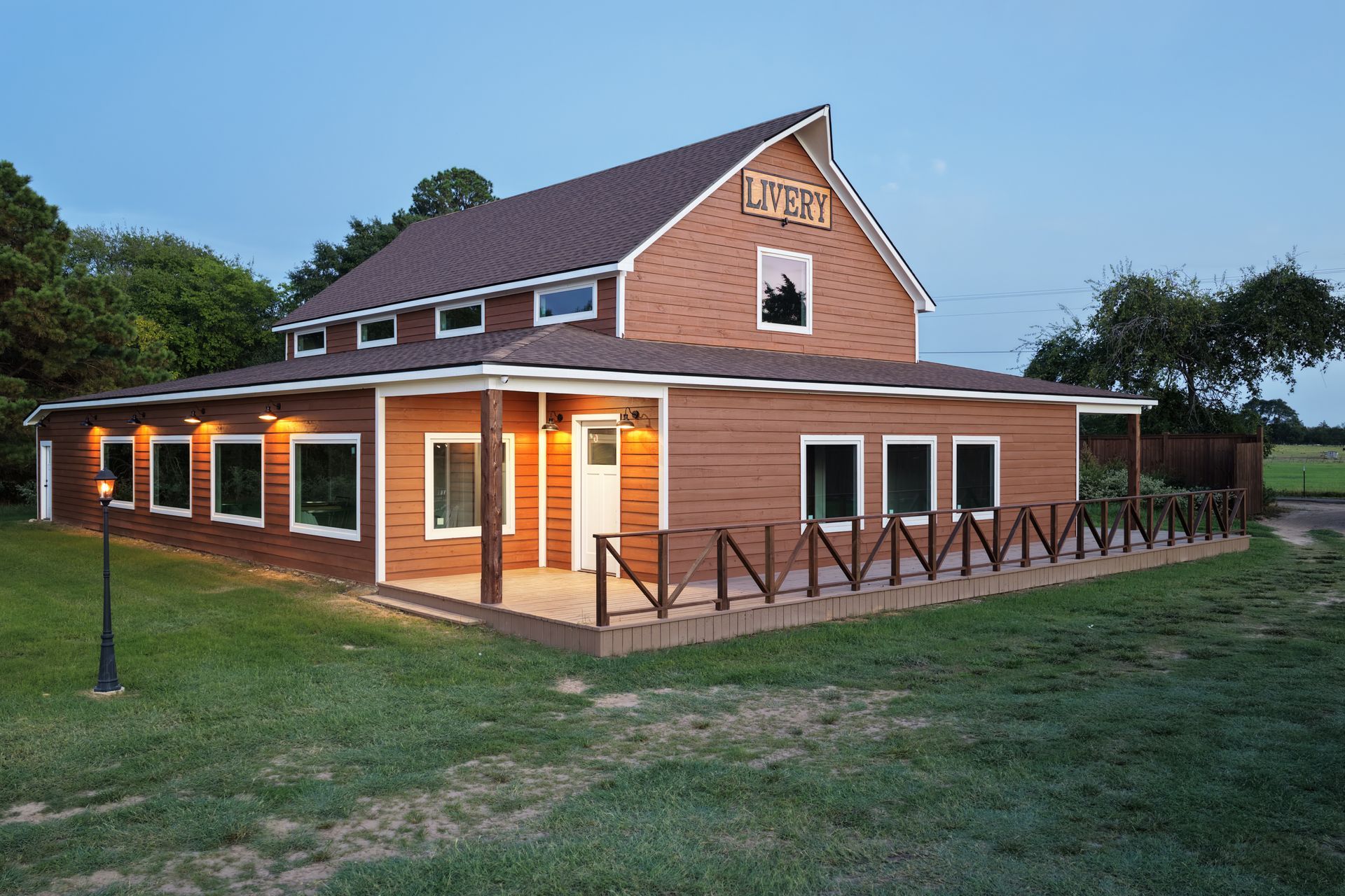 Brick farmhouse with lit porch at dusk, white trim, and fenced yard
