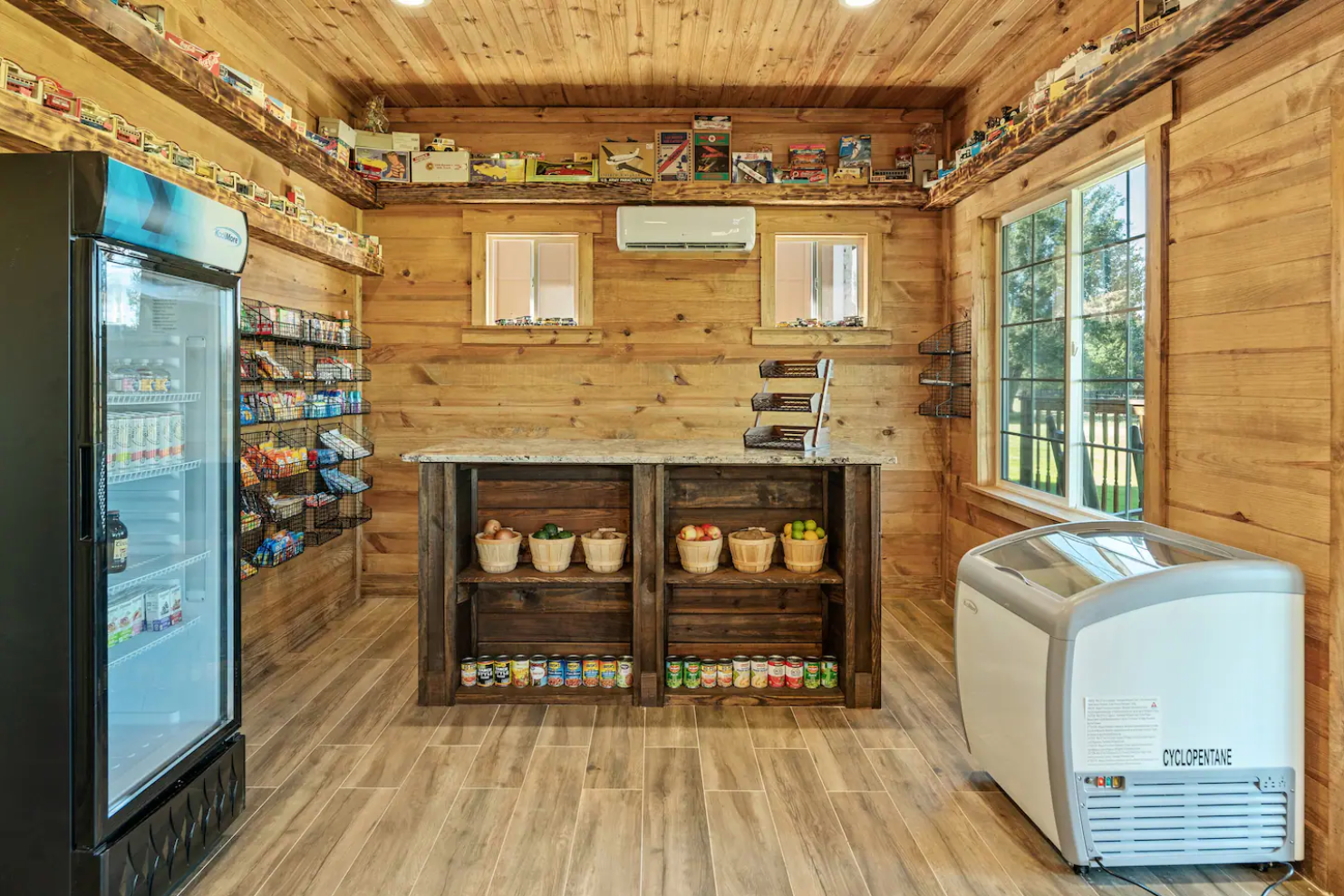 Small rustic store interior with wood walls, a refrigerated drink cooler, a wooden counter, and a chest freezer.
