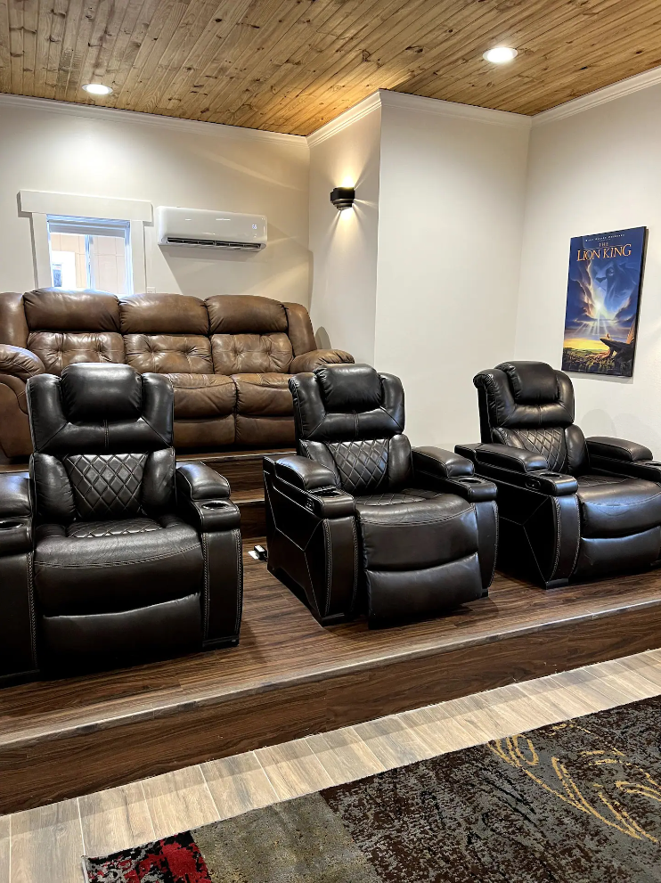 A home theater with three black leather reclining seats on a raised wooden platform in front of a tan leather sofa.