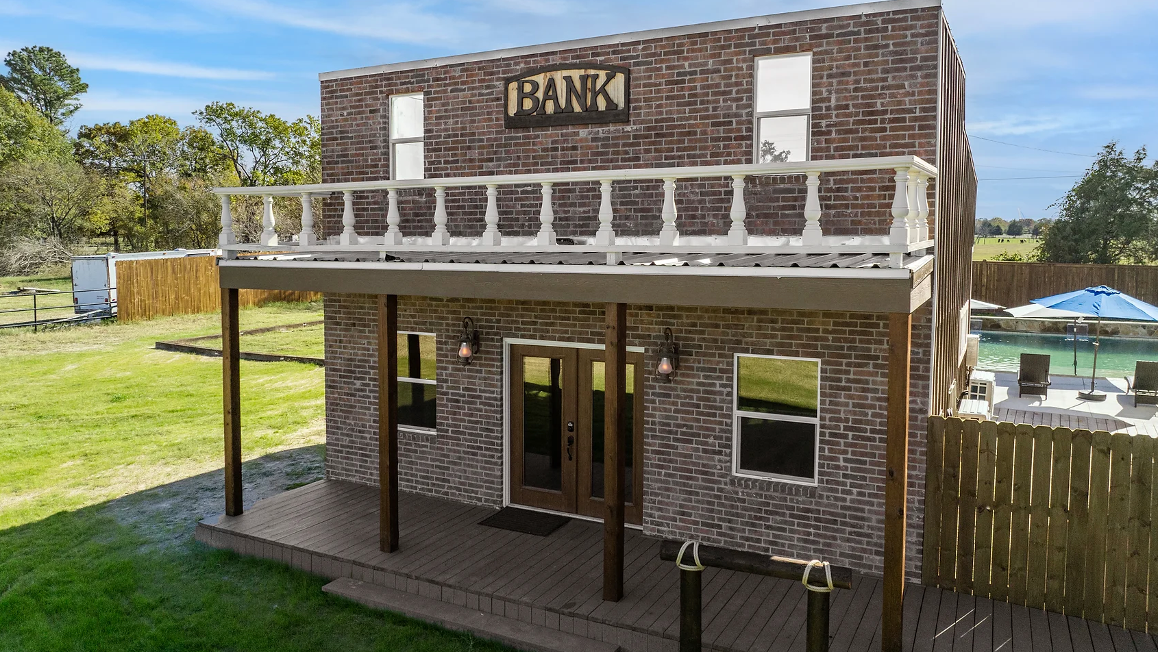 A two-story brick building styled like an old-fashioned western bank with a porch, balcony, and a pool area nearby.